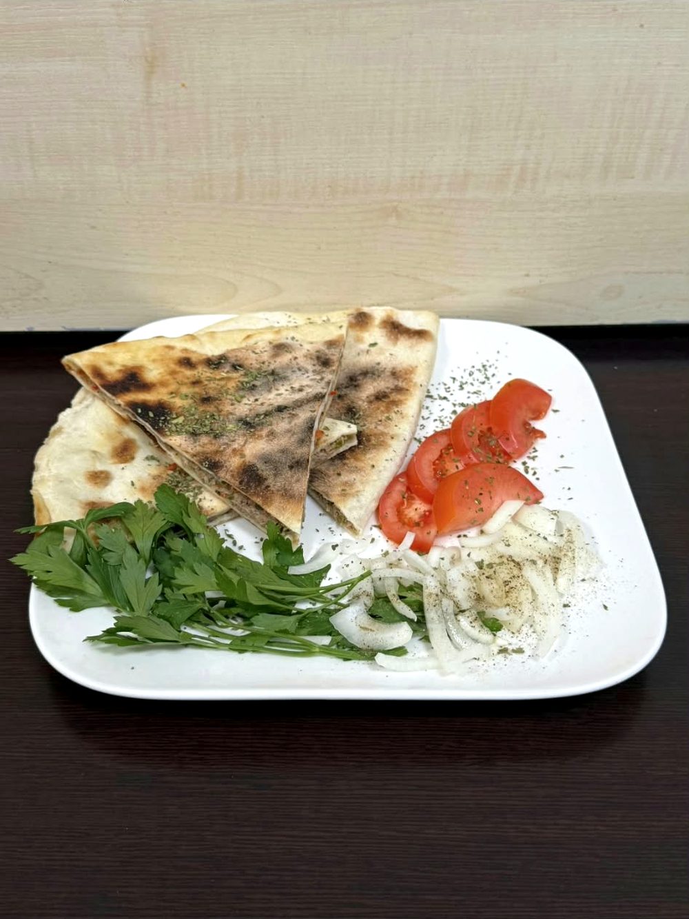Beyaz tabakta kıymalı pide, taze maydanoz, domates ve soğan